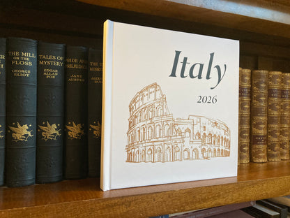 A hardcover travel photobook from There & Back Editions standing upright on a wooden bookshelf next to other antique-style books.
